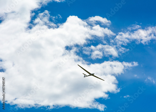 A Glider flying in bleu sky with big white clouds. The glider is a plane that has no engine
