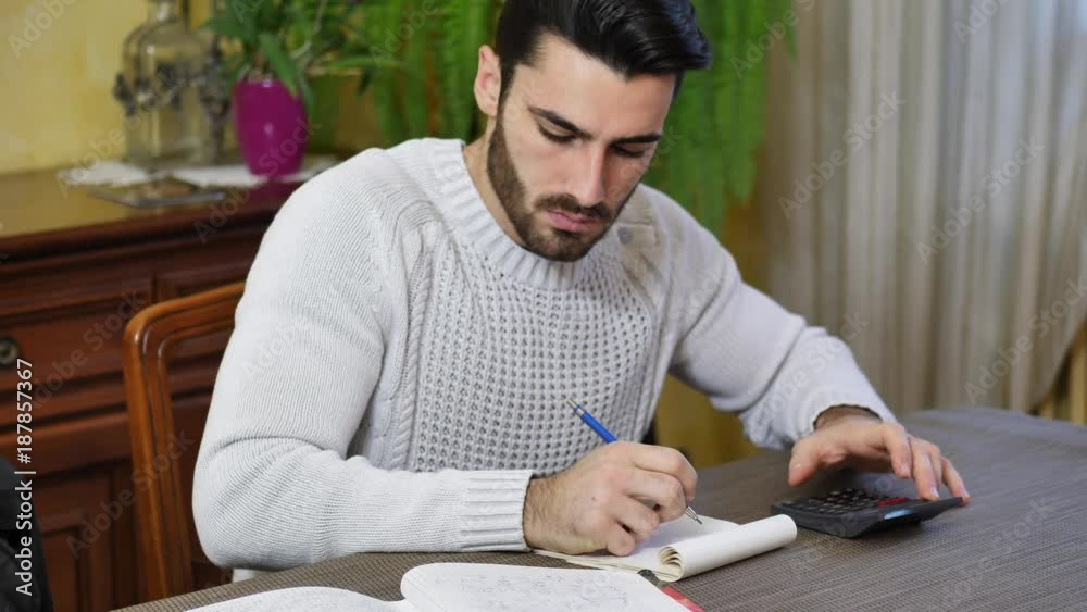 Handsome young man using calculator and accounting at table at home in his living room Handsome young man using calculator and accounting at table at home in his living room