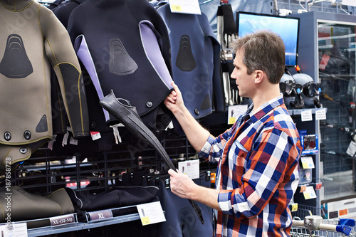 Photography Man chooses wetsuit and fins for spearfishing in sports shop