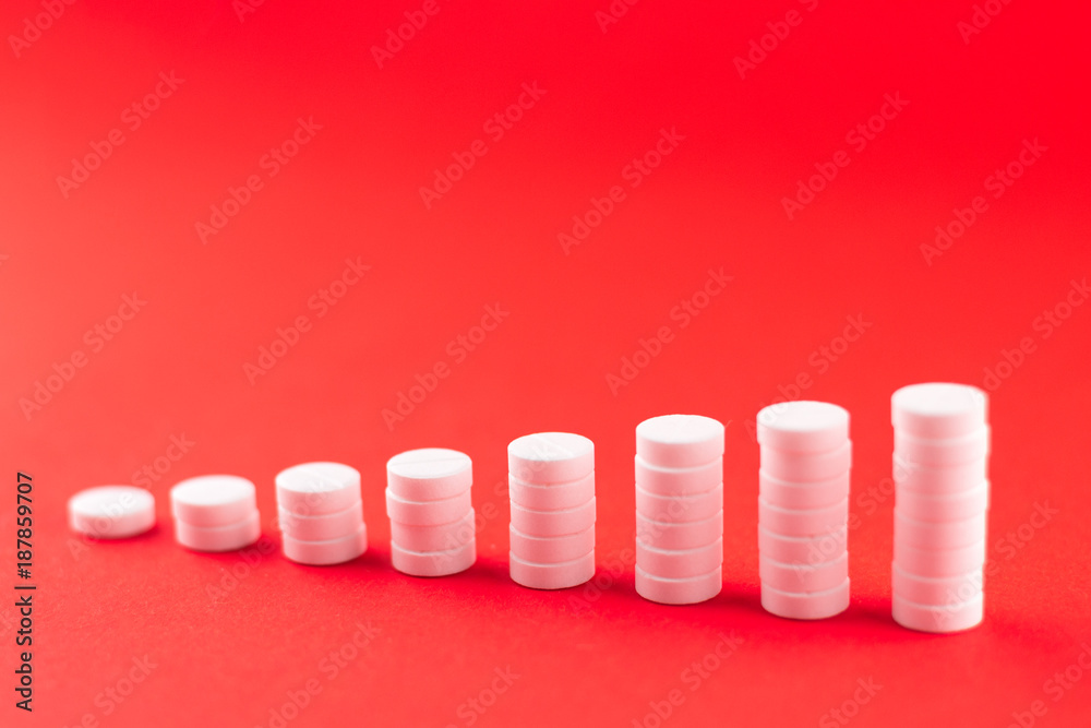 Close up pyramid concept of white pills on scarlet red background with copy space. Focus on foreground, soft bokeh. Pharmacy drugstore concept Close up pyramid concept of white pills on scarlet red background with copy space. Focus on foreground, soft bokeh. Pharmacy drugstore concept