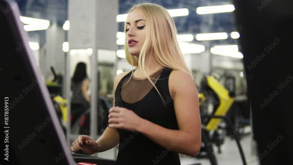 Young attractive blond caucasian woman with piercing in black sport outfit breathing intensly while jogging on treadmill simulator in slomo Young attractive blond caucasian woman with piercing in black sport outfit breathing intensly while jogging on treadmill simulator in slomo
