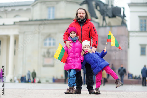 Father and daughters with a flag on Lithuanian independence day holding tricolor Lithuanian flag