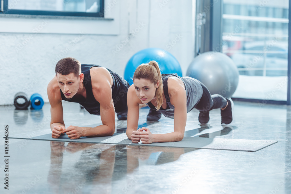 sporty young couple doing plank exercise in gym - obrazy, fototapety, plakaty 