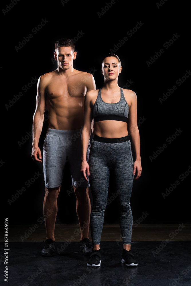 athletic young couple in sportswear looking at camera on black