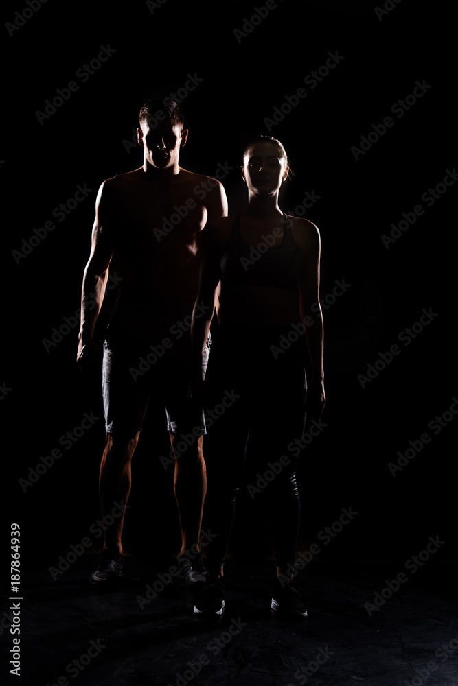 silhouettes of athletic young couple standing together on black