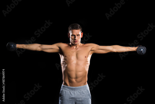muscular shirtless sportsman holding dumbbells and looking at camera isolated on black