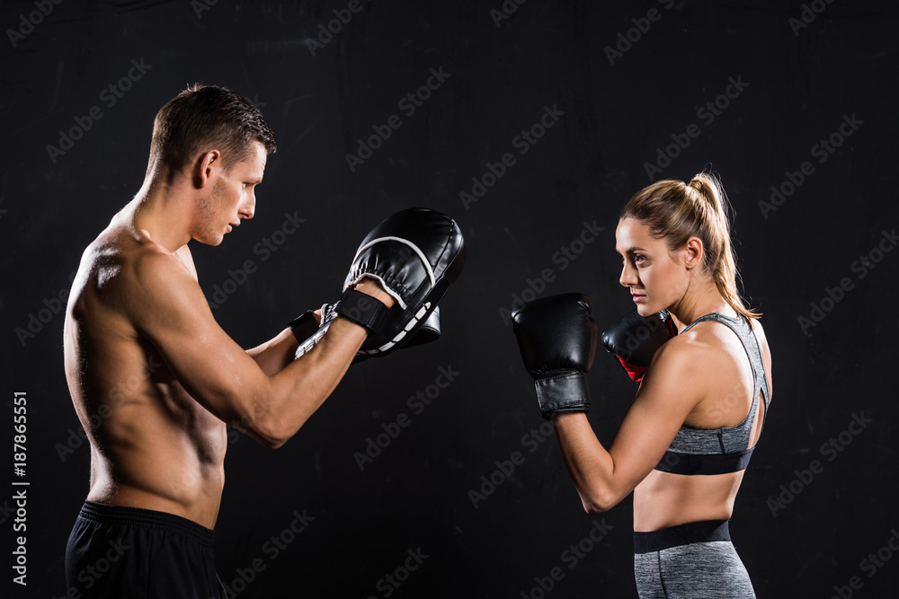 Plakat side view of sporty young couple boxing isolated on black