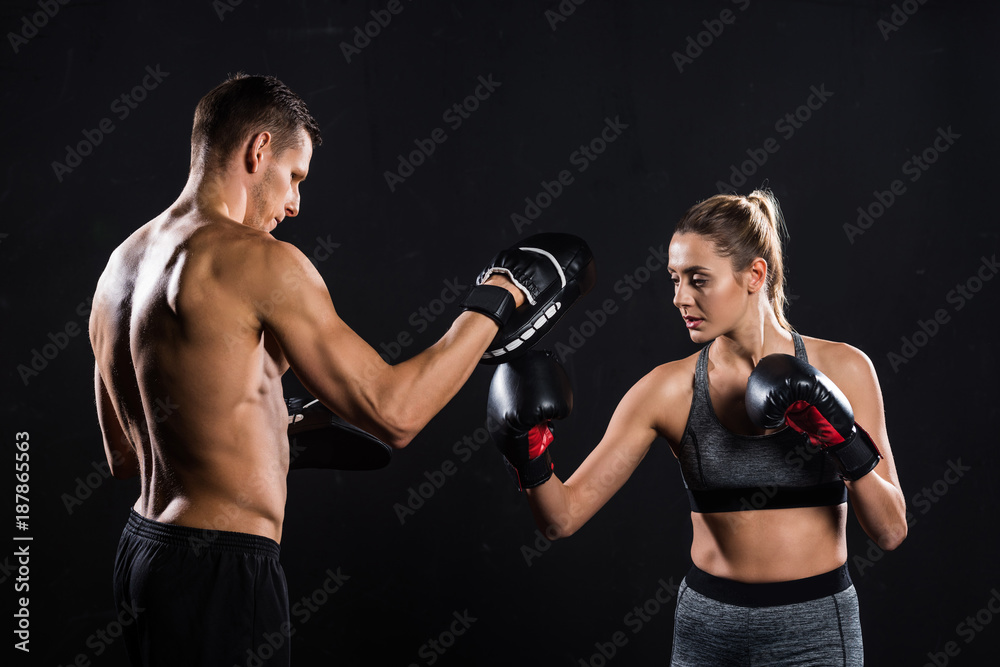 Plakat side view of athletic young couple boxing isolated on black