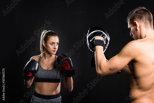 cropped shot of shirtless trainer exercising with female boxer isolated on black