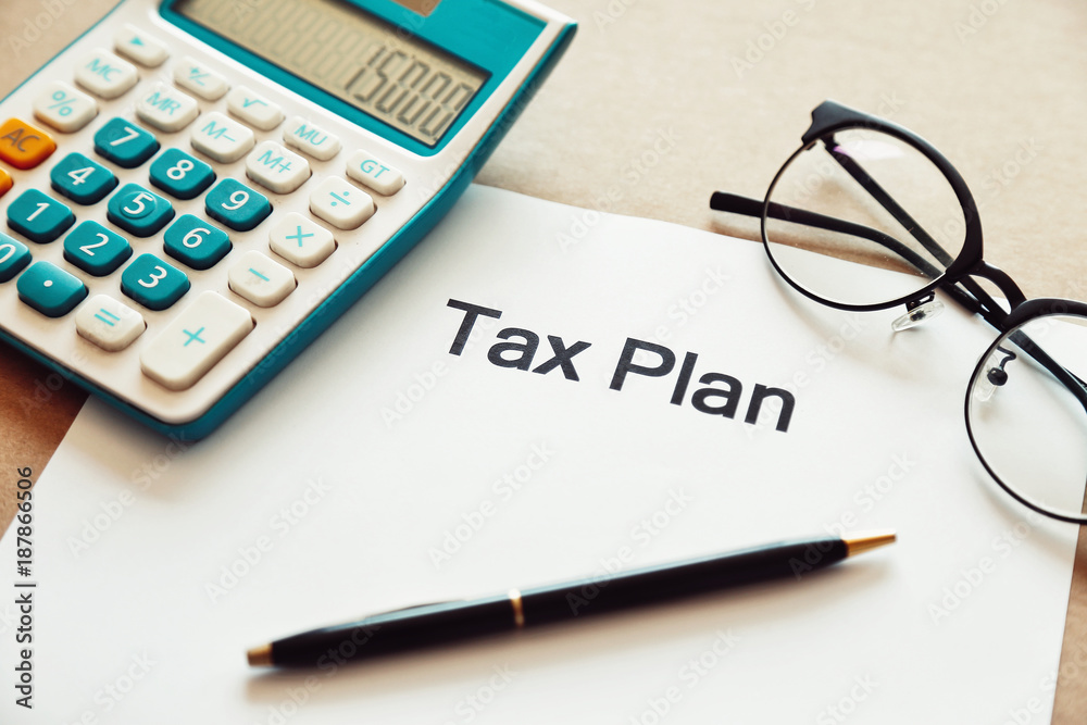 Close up tax planning word on paper with calculator, pen and eye glasses place on the wooden table. Close up tax planning word on paper with calculator, pen and eye glasses place on the wooden table.