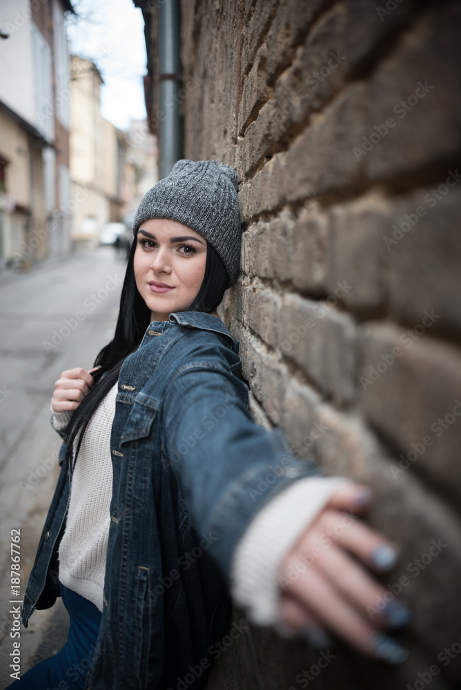 young woman reaching with hand to you while leaning on brick wall 