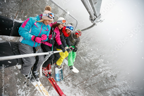 happy friends skiers and snowboarders on ski lift for skiing in the mountains