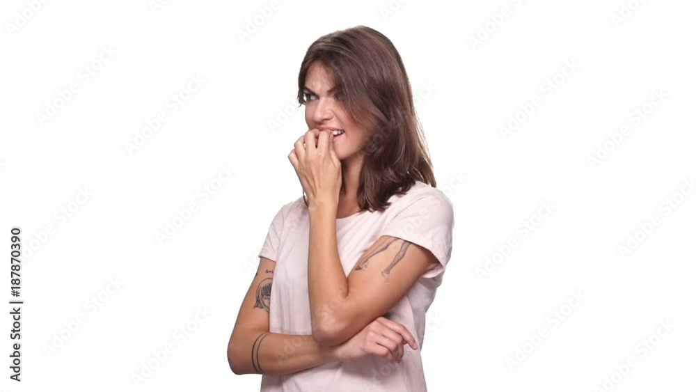 Worried brunette woman in t-shirt bites her fingers and looking around over white background Worried brunette woman in t-shirt bites her fingers and looking around over white background
