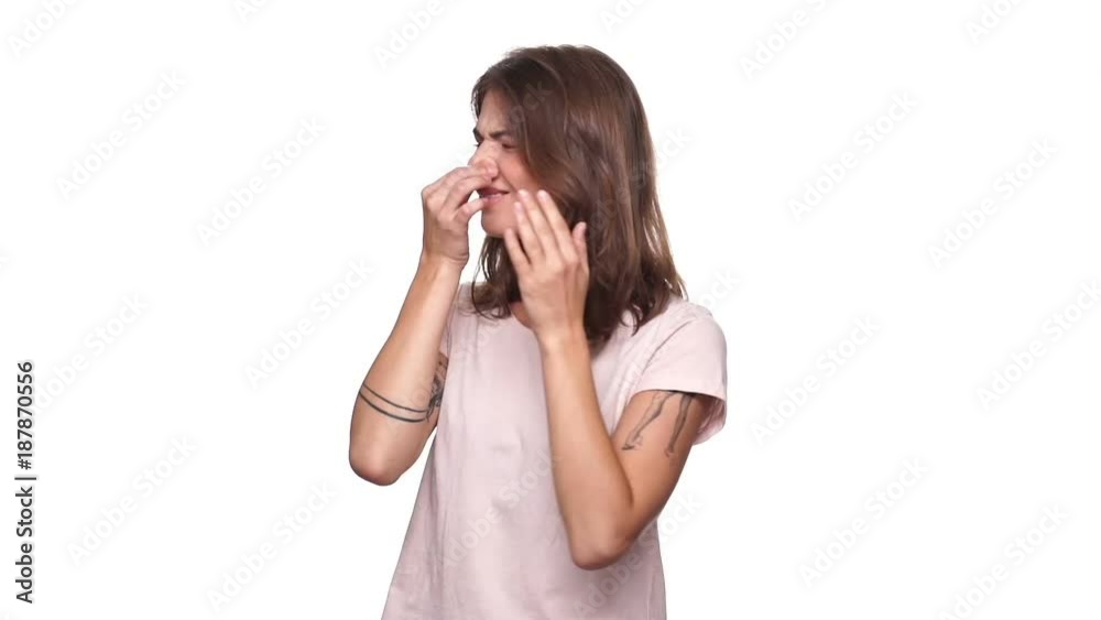 Confused brunette woman in t-shirt covering her nose because of stink around over white background Confused brunette woman in t-shirt covering her nose because of stink around over white background