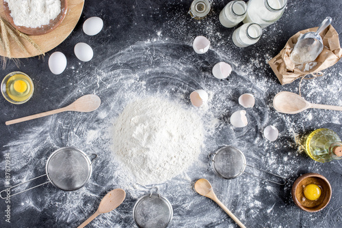 flat lay with flour and other ingredients for bakery, wooden kitchenware on dark tabletop
