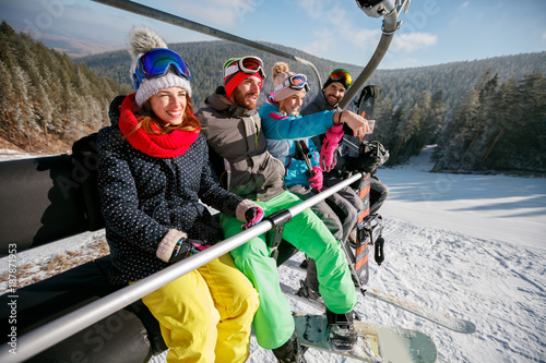 Smiling friends skiers and snowboarders on ski lift in the mountain