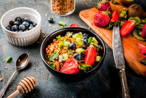 Healthy breakfast with muesli or granola with nuts and fresh berries and fruits - strawberry, blueberry, kiwi, on dark blue table, copy space
