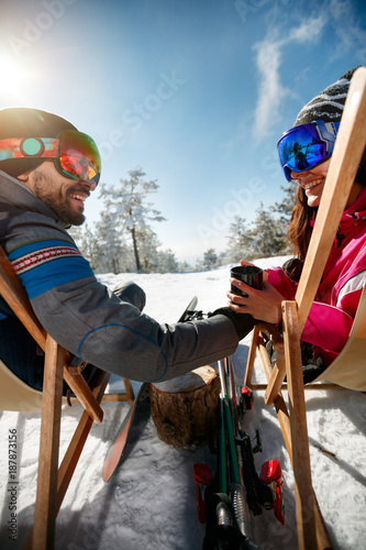 Couple spending time together and drink after skiing in ski resort. Back view