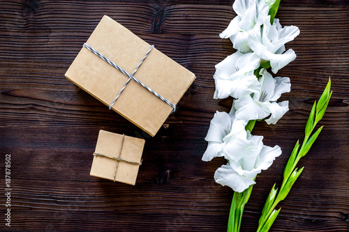 Gift box wrapped in craft paper near flower gladiolus on wooden 