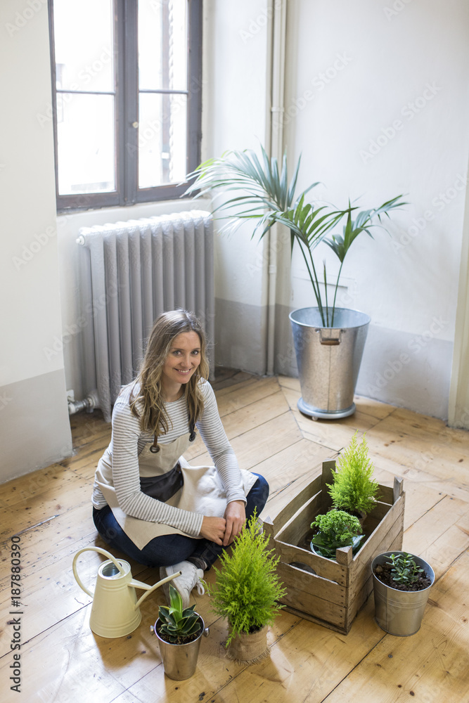 Portrait of smiling woman sitting on floor at home caring for plants Portrait of smiling woman sitting on floor at home caring for plants