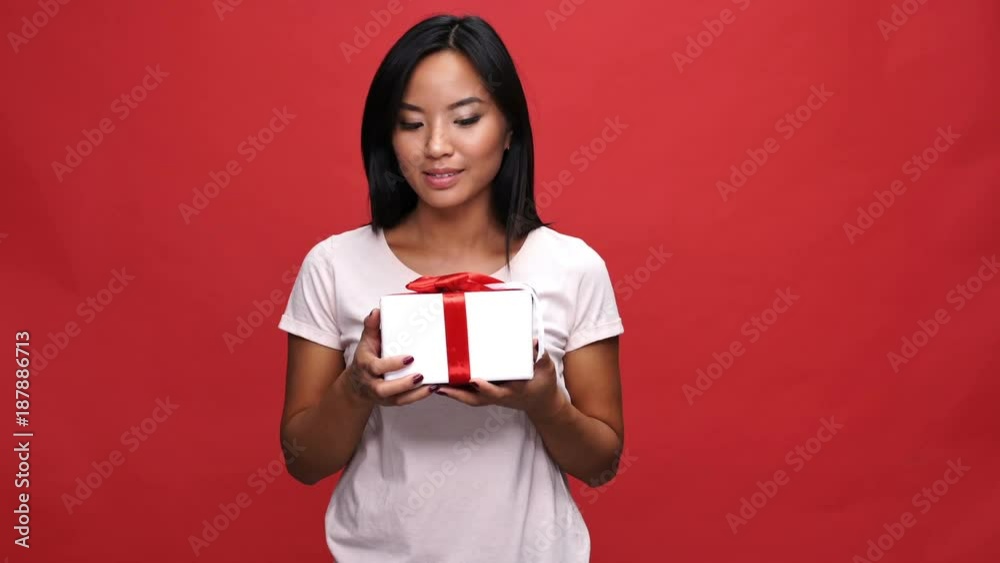 Pleased intrigued asian woman in t-shirt holding gift box over red background
Pleased intrigued asian woman in t-shirt holding gift box over red background