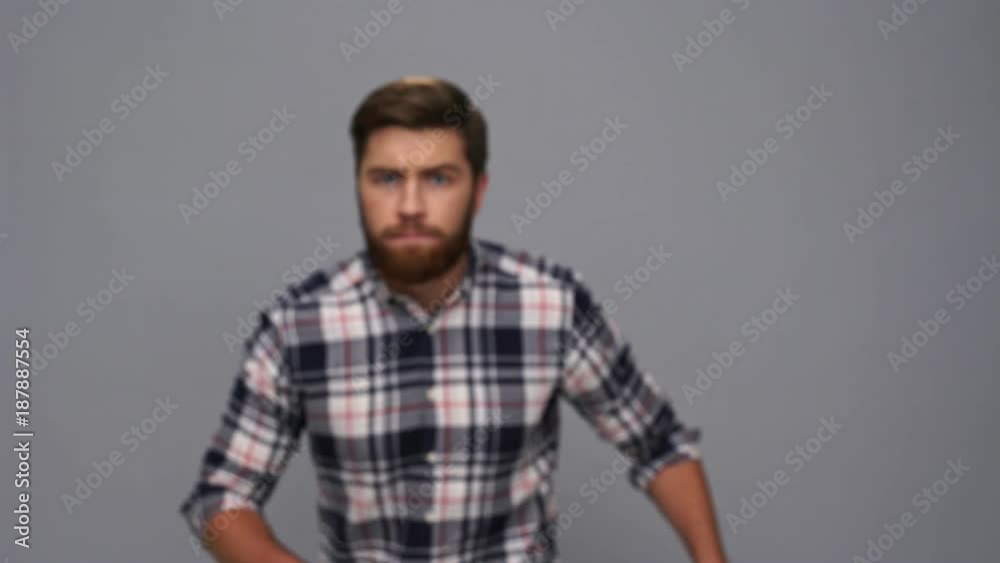 Mystery bearded man in shirt sneaks, looking at the camera and running away after that over gray background Mystery bearded man in shirt sneaks, looking at the camera and running away after that over gray background