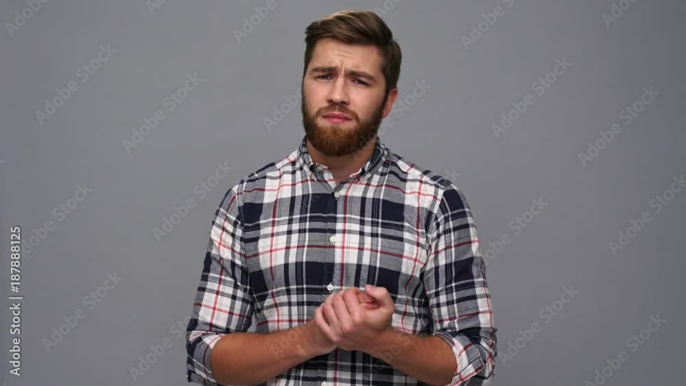 Confused bearded man in shirt upset and looking down over gray background Confused bearded man in shirt upset and looking down over gray background