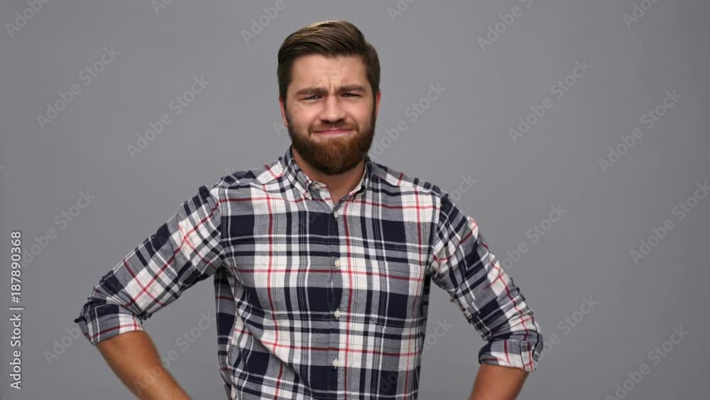 Displeased bearded man in shirt showing thumb down over gray background Displeased bearded man in shirt showing thumb down over gray background