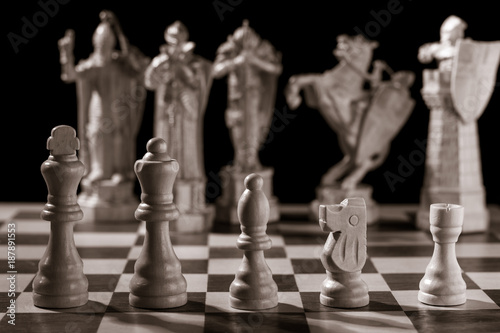 Classic white chess pieces and the same pieces in the form of medieval figures on the background