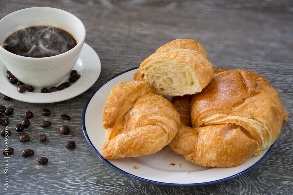 Butter Croissants in white dish and hot black coffee in the cup and coffee seeds on wooden table Butter Croissants in white dish and hot black coffee in the cup and coffee seeds on wooden table