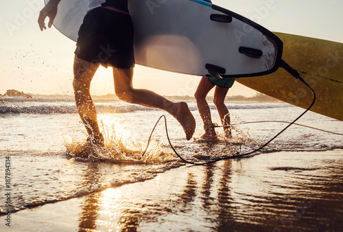 Photography Son and father surfers run in ocean waves with long boards