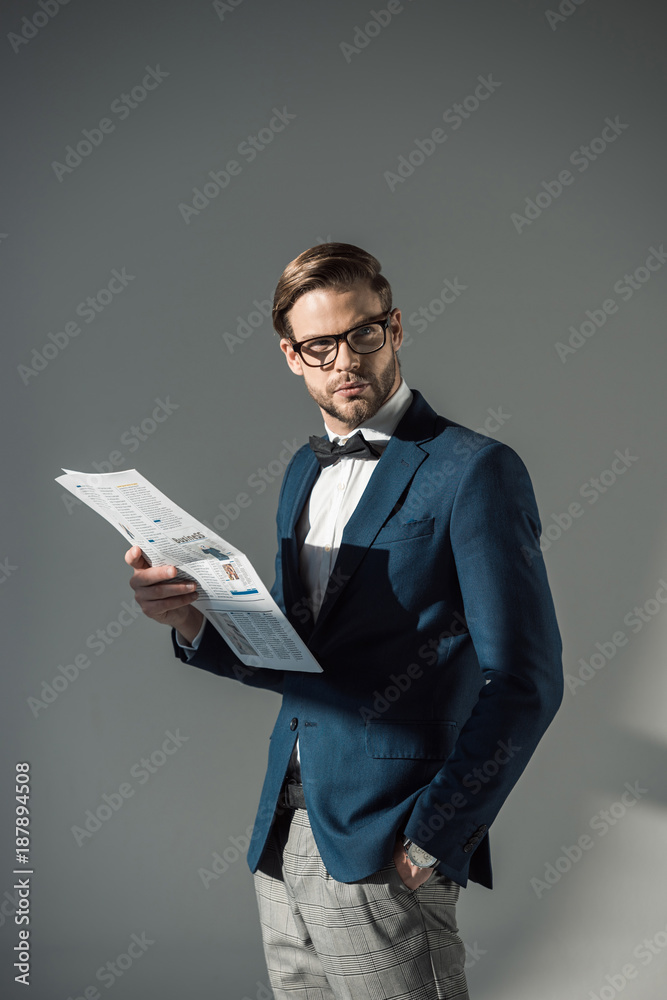 portrait of handsome fashionable businessman in spectacles reading newspaper on grey