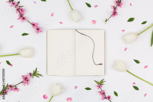 drawing, organisation, femininity concept. top view of opened clean sketchbook with purple silk ribbon as bookmark, it is placed among delicate white tulips and pink oriental cherry photo