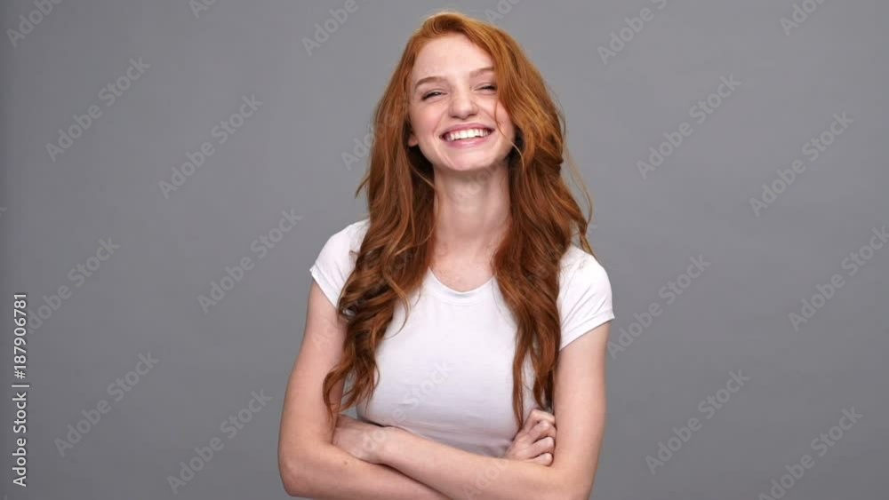Laughing ginger woman in t-shirt holding crossed arms and looking at the camera over gray background Laughing ginger woman in t-shirt holding crossed arms and looking at the camera over gray background