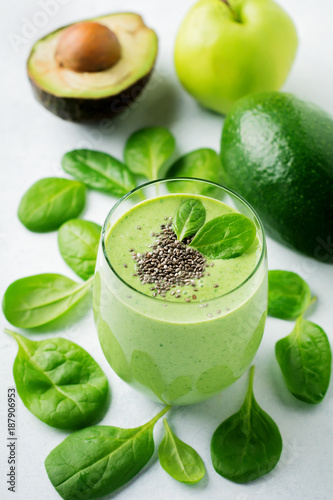 Vegetarian healthy green smoothie from avocado, spinach leaves, apple and chia seeds on gray concrete background. Selective focus. Space for text.