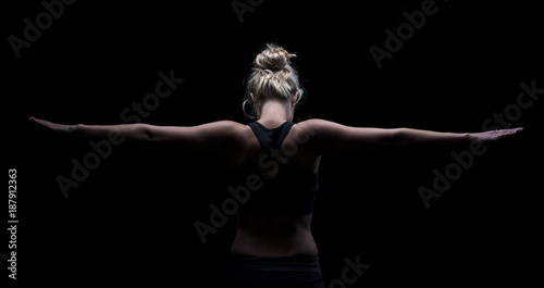 Beautiful fit and healthy blond woman in black top in dark with arms stretched from behind