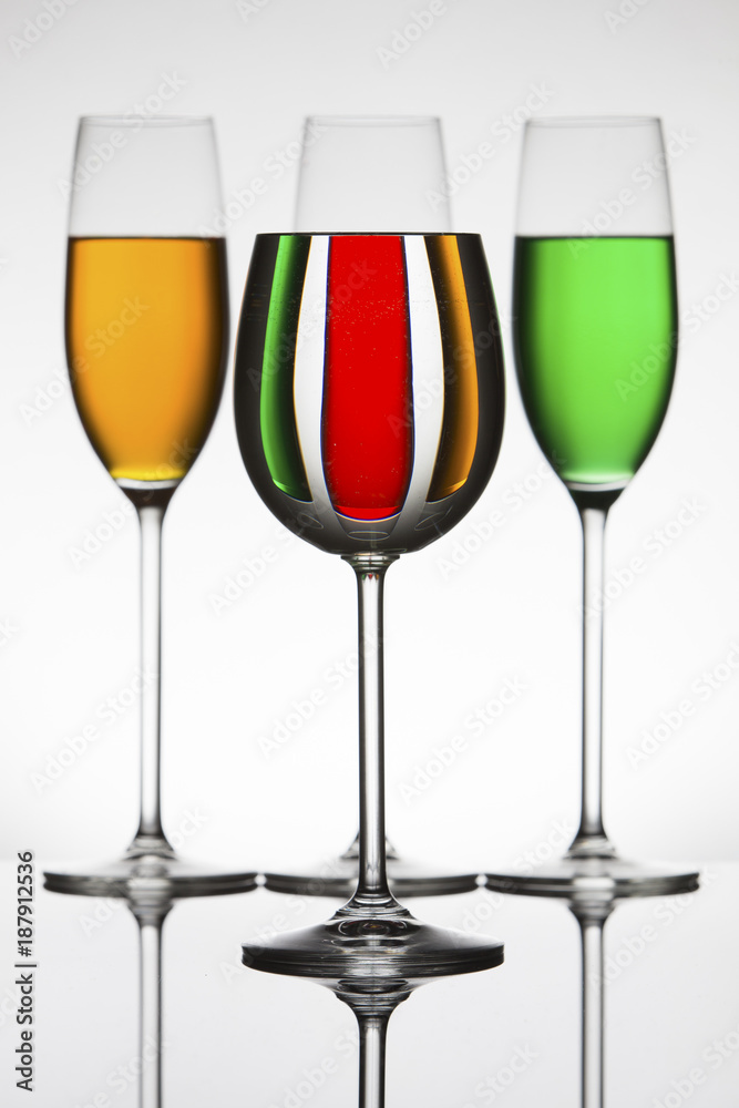 Wineglasses on a shiny surface with different colour fluids that distort reflection Wineglasses on a shiny surface with different colour fluids that distort reflection
