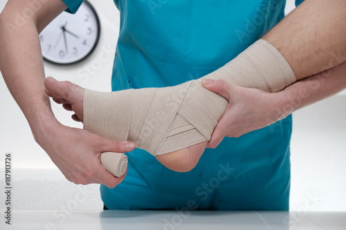 Billede på lærred Close-up of male doctor bandaging foot of female patient