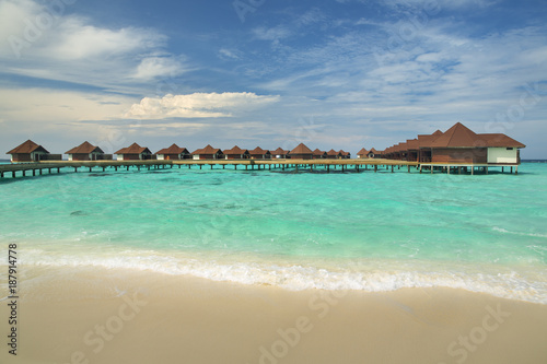 sea view to white wave on the beach and emerald water with bungalows above the water on Maldives island