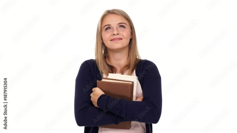 Pleased pensive blonde woman in cardigan holding books and looking up over white background Pleased pensive blonde woman in cardigan holding books and looking up over white background