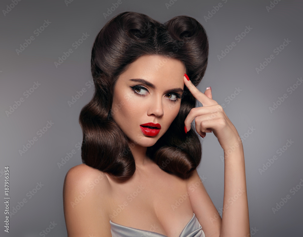 Pin up girl with red lips makeup and retro curls hair style. Retro woman  looking to the side holds a finger near the head. Expressive facial  expressions. High fashion photo. Stock Photo |