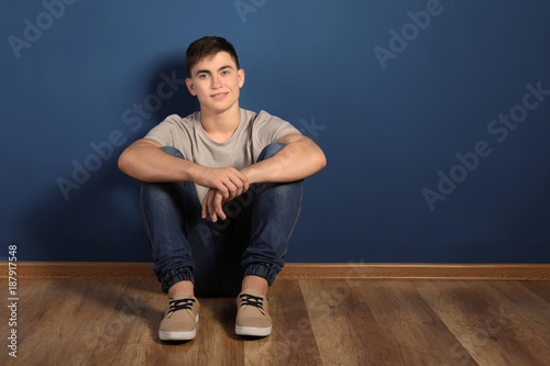 Trendy teenage boy sitting on floor near color wall