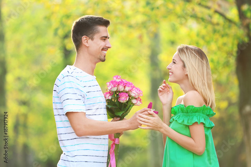 Young man with engagement ring and flowers making proposal of marriage to his girlfriend in park