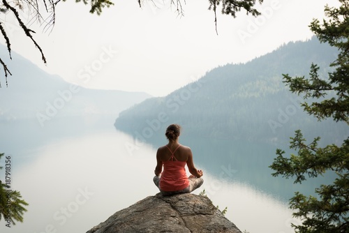 Fit woman sitting in meditating posture on the edge of a rock photo