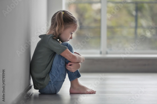Foto Sad little girl sitting on floor indoors