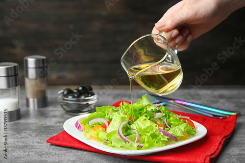 Woman adding tasty apple vinegar to salad with vegetables on table