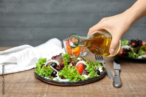 Schilderij op canvas Woman adding tasty apple vinegar to salad with vegetables on table
