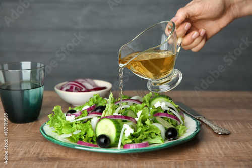 Woman adding tasty apple vinegar to salad with vegetables on table photo