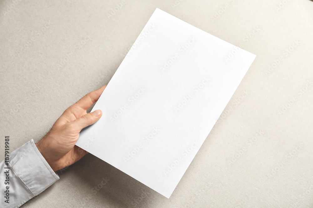 Fototapeta premium Man holding blank sheet of paper on light background. Mock up for design