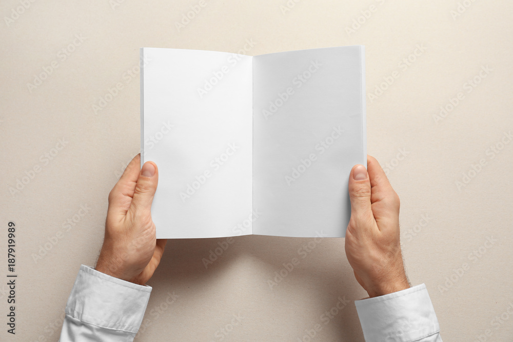 Obraz premium Man holding brochure with blank pages on light background. Mock up for design
